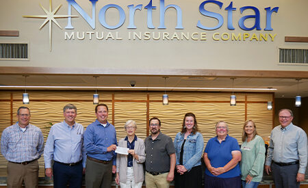 Nine people stand in a row holding a check beneath a North Star Mutual Insurance Company sign.