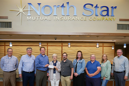 Nine people stand in a row holding a check beneath a North Star Mutual Insurance Company sign.