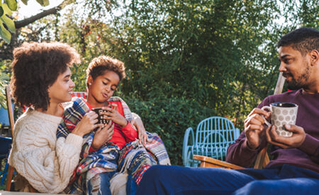 A family relaxes outside, wrapped in blankets and enjoying hot drinks together.